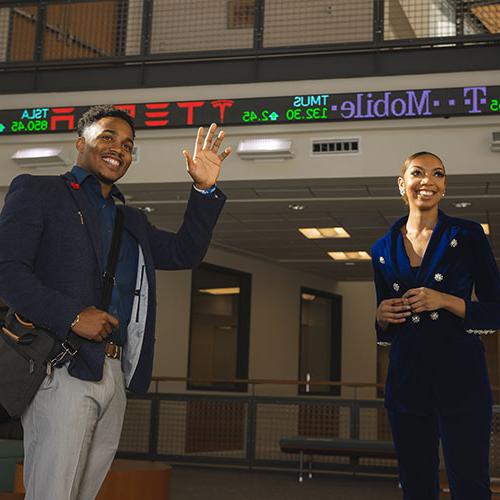two students in the college of business atrium underneath the stock ticker