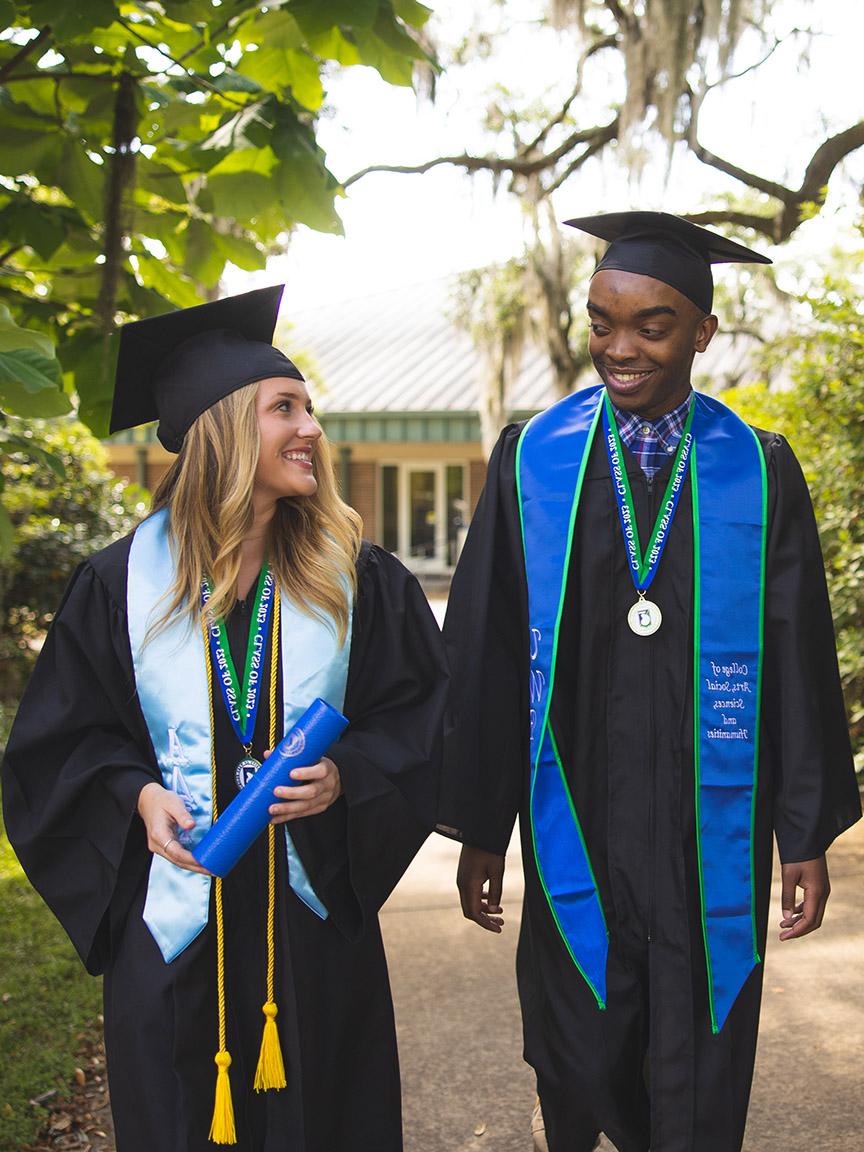 UWF graduates walk together in cap and gown.