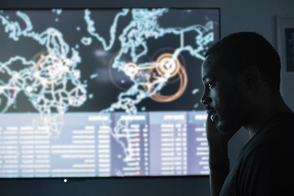 cybersecurity student in front of a large cyber threat dashboard